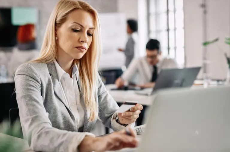 Mulher olhando para cartão de crédito e escrevendo no computador