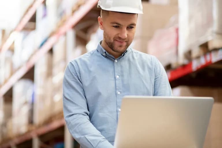 Homem utilizando notebook em galpão de armazenamento