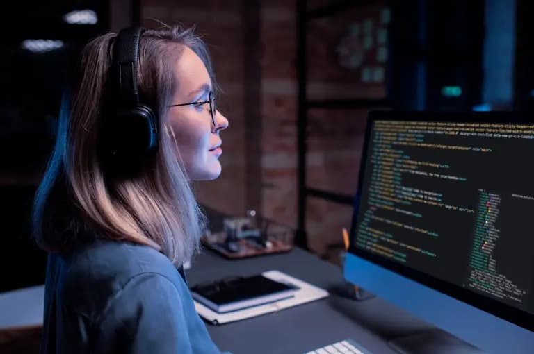 Mulher ruiva jovem trabalhando com programação em 3 monitores